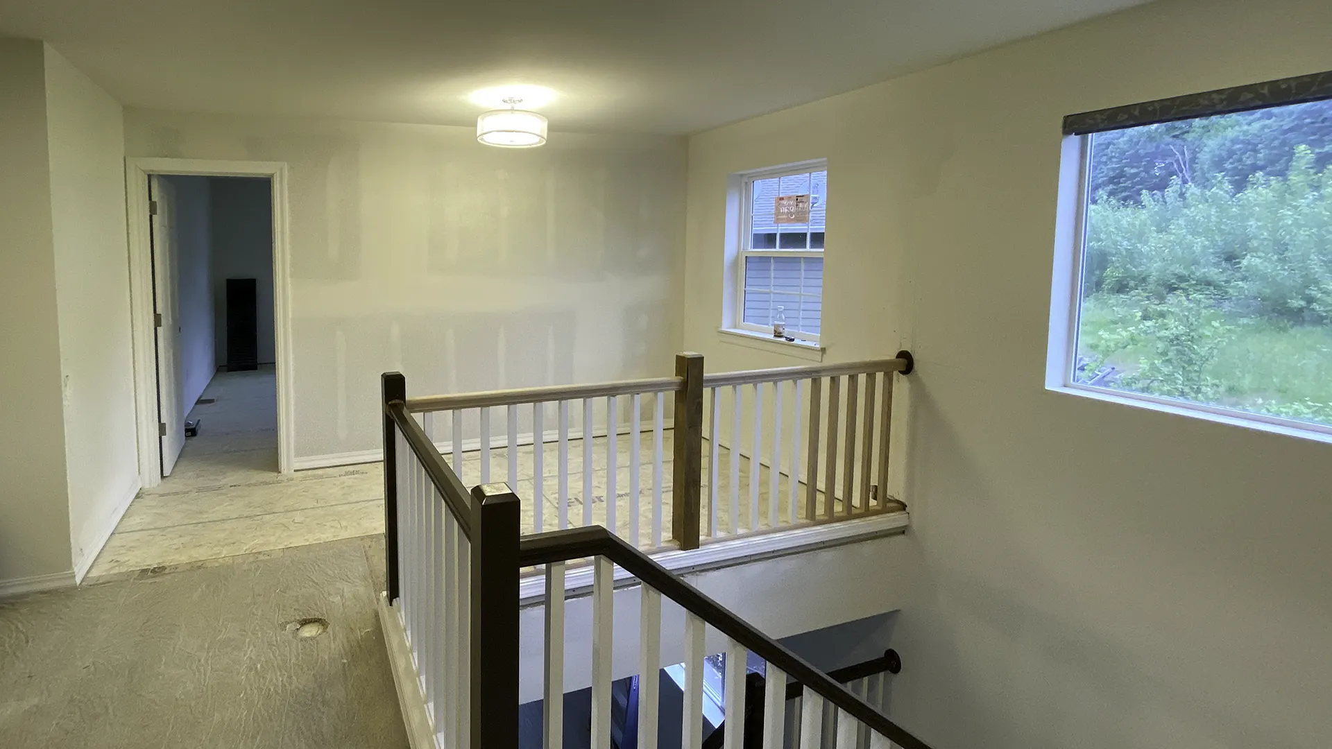 New upstairs hallway with bedroom door, window, and staircase railing