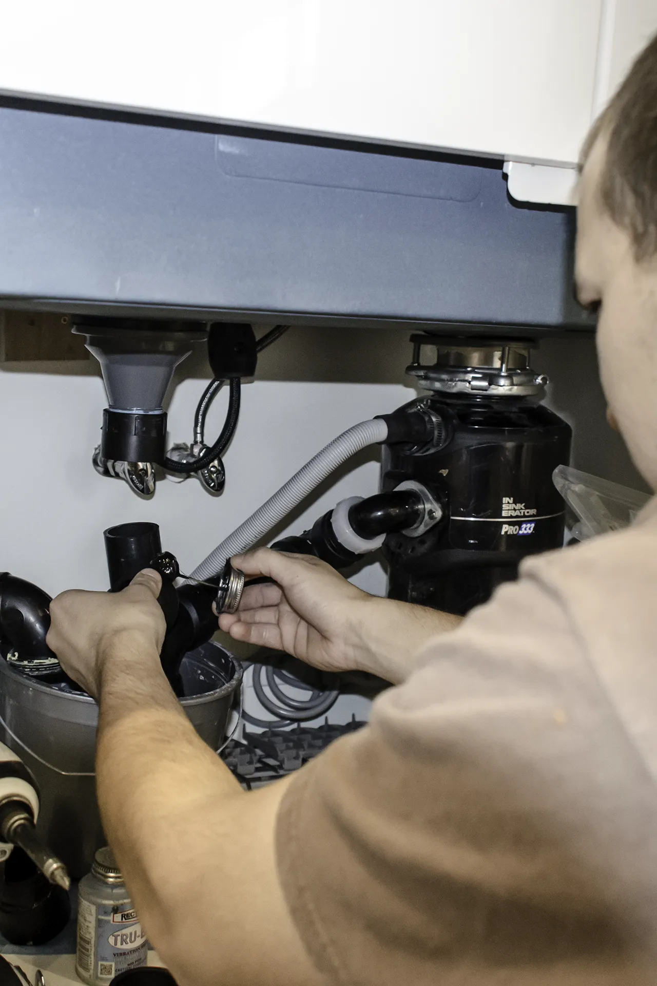 Plumber connecting garbage disposal and drain lines under an IKEA kitchen sink